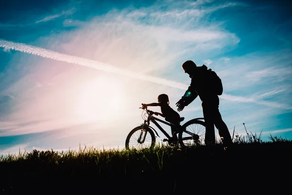 Pai ajudar pequena filha para andar de bicicleta ao pôr do sol natureza — Fotografia de Stock