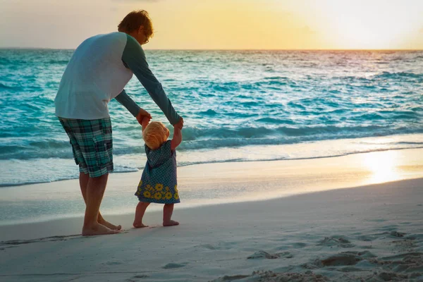 Otec a malá dcera dělat první kroky na pláži západ slunce — Stock fotografie