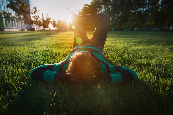 Молодий чоловік відпочиває на зеленій траві на заході сонця — стокове фото
