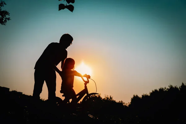 Pai ensinando filhinha a andar de bicicleta ao pôr do sol natureza — Fotografia de Stock