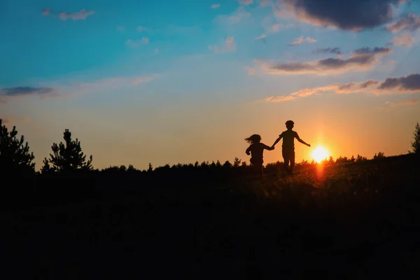 Silhouette de garçon et fille heureux courir au coucher du soleil — Photo