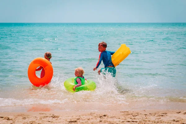 Happy boy and girls with floaties run swim on beach — Stock Photo, Image