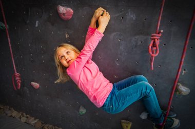 Spor salonunda yapay kaya duvarına tırmanan tatlı bir kız.