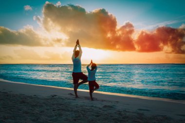 Baba oğul gün batımı kumsalında egzersiz, aile yoga yapıyor.
