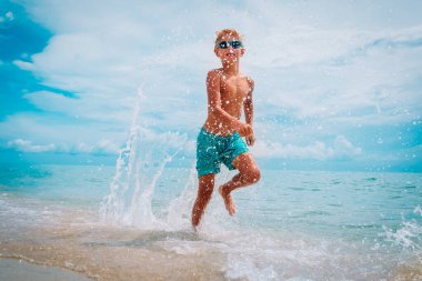 Mutlu çocuk sahilde koşup su sıçratıyor.