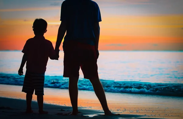 Silhouet van vader en zoon hand in hand bij zonsondergang zee — Stockfoto