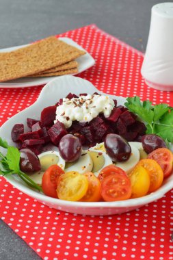 Kolay Kahvaltı: beetroots, kiraz domates, yumurta, peynir ve kraker kırmızı Tekstil arka plan üzerinde beyaz bir tabak içinde. Sağlıklı gıda kavramı