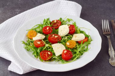 Kiraz domates, mozzarella peyniri, ruccola zeytinyağı şarap sirke gri bir arka plan üzerinde beyaz bir plaka üzerinde geleneksel İtalyan salatası