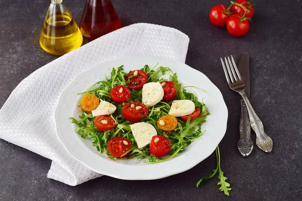 Traditional Italian salad with cherry tomato, ruccola, mozzarella, olive oil wine vinegar on a white plate on a grey abstract background — Stock Photo, Image