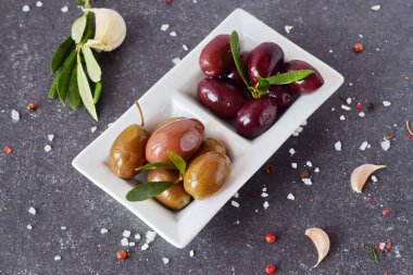 Limon, sarımsak, baharatlar ile gri bir arka plan üzerinde beyaz bir tabak içinde siyah ve yeşil zeytin. Akdeniz yemekleri. Sağlıklı beslenme kavramı.