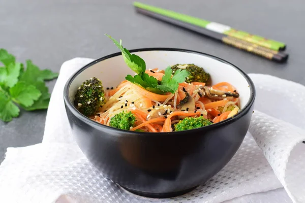 Рисовая лапша с морковью, брокколи и грибами в черной миске на черном абстрактном фоне. Азиатская еда. Здоровое питание . — стоковое фото