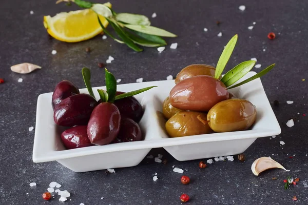 Черные и зеленые оливки в белой тарелке на сером абстрактном фоне с лимоном, чесноком, специями. Средиземноморская Концепция здорового питания . — стоковое фото