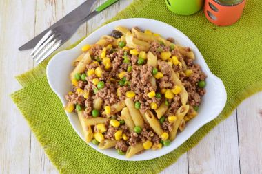 Kıyılmış et, yeşil bezelye ve beyaz bir tabak içinde sarı Mısır ile makarna. Ev yemekleri. Sağlıklı beslenme kavramı.