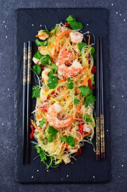 Karides ve gri bir arka plan üzerinde siyah taş tabakta sebze erişte. Sağlıklı gıda kavramı.