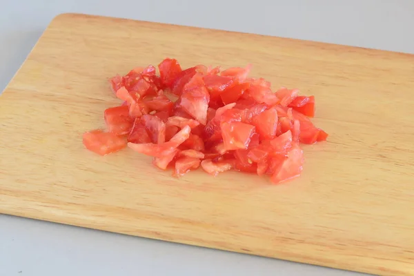 Cozinhar passo a passo. Tomate fresco picado sobre uma tábua de corte de madeira sobre fundo cinzento . — Fotografia de Stock