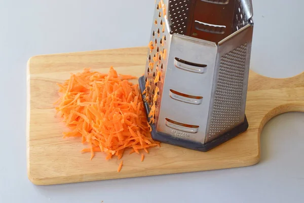Шаг за шагом готовка. Тертая морковь с теркой на деревянной доске для резки на сером фоне . — стоковое фото