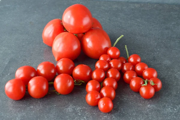 Diversi tipi di pomodori su rami con rosmarino e sale marino su fondo grigio scuro astratto. Alimentazione sana concetto . — Foto Stock