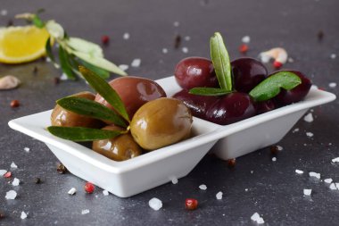 Limon, sarımsak, baharatlar ile gri bir arka plan üzerinde beyaz bir tabak içinde siyah ve yeşil zeytin. Akdeniz yemekleri. Sağlıklı beslenme kavramı.