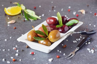 Limon, sarımsak, baharatlar ile gri bir arka plan üzerinde beyaz bir tabak içinde siyah ve yeşil zeytin. Akdeniz yemekleri. Sağlıklı beslenme kavramı.