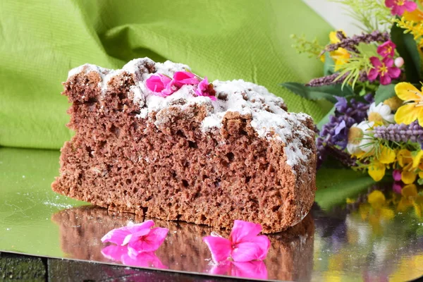 Un morceau d'un délicieux gâteau au chocolat fait maison sur une assiette d'argent avec des fleurs et un tissu vert comme fond. Cuisine maison. Célébrations, Vacances, Gâteau d'anniversaire . — Photo