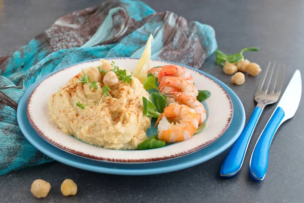 Purée de pois chiches à la crème et au beurre servie avec des crevettes bouillies sur une assiette blanche et bleue sur un fond abstrait gris. Une nourriture saine. Concept de saine alimentation . — Photo