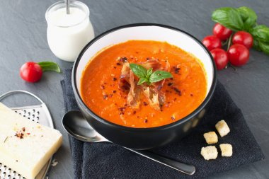 Fesleğen ve gri bir arka plan üzerinde siyah bir seramik kase kızarmış domuz pastırması ile kalın domates çorbası. Sağlıklı beslenme kavramı