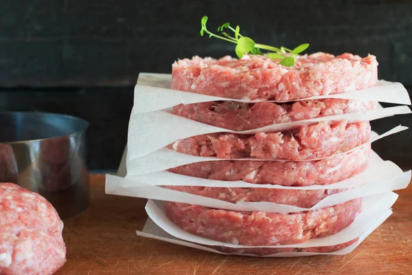 Stapel rauwe zelfgemaakte rundvlees hamburgers op een houten snijplank met enkele gehakt vlees en metal vorm op een achtergrond. Thuis gezond eten. — Stockfoto