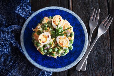 Haşlanmış havuç, bezelye, yumurta, peynir ve yohurt ve ahşap bir zemin üzerine mavi bezle mavi tabakta sarımsak ile taze kırmızı soğan salatası.