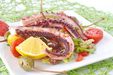 Ahtapot zeytin yağı zeytin, kekik, domates, Kapari, limon beyaz tabakta ile pişirilir. Sağlıklı beslenme.