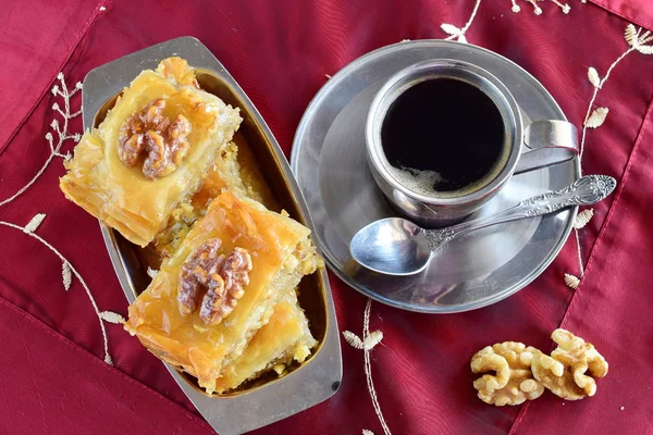 Traditional Greek baklava made with filo dough, sugar syrup and wallnuts on a metal tray with metal coffee cup on a purple cloth background. — Stock Photo, Image