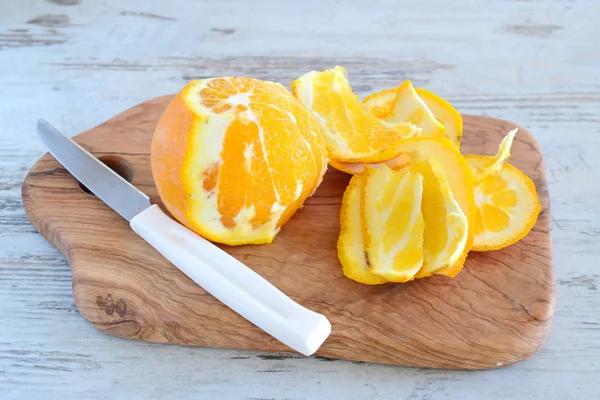 Peeling of orange on a olive wood cutting board on a grey background. Step by step cooking. — Stock Photo, Image