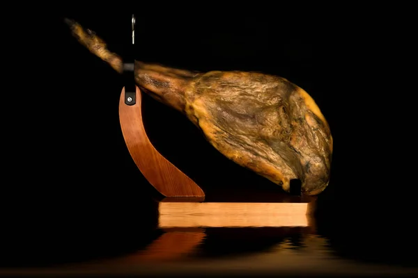 Pierna entera de jamón ibérico en un soporte de jamón reflejado en negro —  Fotos de Stock