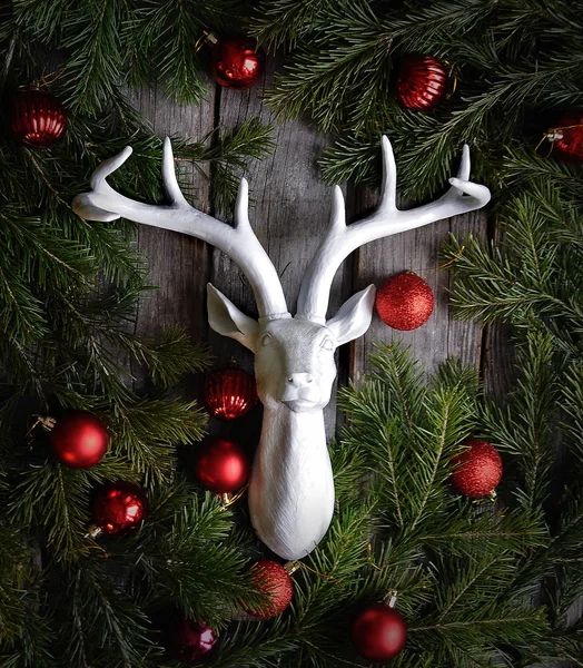 sculpture a white deer head on a dark wooden background with a Christmas tree wreath and bright red happy new year decorations in vintage style