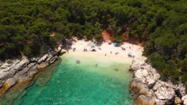 İnsansız hava aracı Kimilia, Kefalonia, Yunanistan üzerinde uçuyor. Hava görüntüleri, stok videoları. İnsansız hava aracı küçük sahil ve denizin üzerinde geriye doğru uçuyor. Okyanusta yüzen insanlar var.