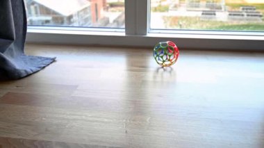 Bebekler, çocuklar ya da evcil hayvanlar için renkli plastik top, ağır çekimde ahşap bir salonun zemininde yuvarlanıyor. Top panorama penceresine çarptı ve geri sekti. Durmadan önce etrafında dönüyordu. Brian Holm Nielsen 'in stok video görüntüleri.