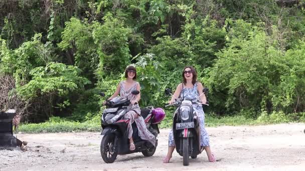 Милі дівчата і мотоцикли/скутери говорити і посміхається. Азіатський тропічних рослин і дерев на тлі. Острів Балі, Індонезія. 1080 р, 50 кадрів в секунду, повний голова азіатських лісові фону. — стокове відео