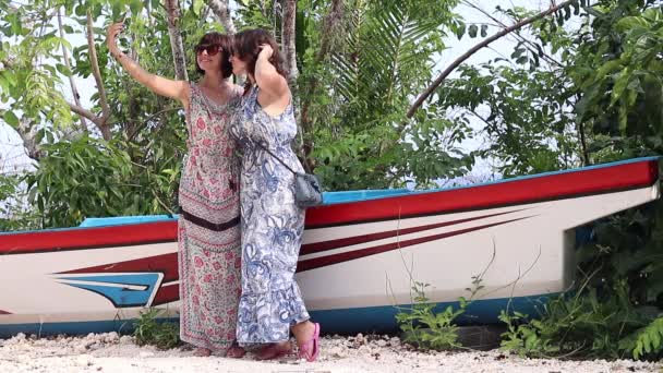 Dos jóvenes muy sexy damas tomando una selfie juntos cerca de las plantas exóticas y el viejo barco. Sonriendo y riendo, siéntete feliz. Vacaciones en la isla de Bali, Indonesia. Autorretrato, hermosa vista . — Vídeo de stock