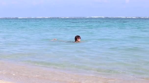布鲁内特年轻性感的女人游泳在巴厘岛的海洋，印度尼西亚。慢动作，全高清，50 fps。在海滩上享受女性健康的生活方式. — 图库视频影像