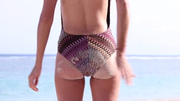 Zadní pohled sexy krásná mladá žena, která otírala plážový písek z prdele pomalý pohyb, tropický oceán. Bali, Indonésie. Atraktivní ženské tělo, štíhlá dívko. Zpomaleně. Oceán na pozadí. — Stock video