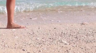 Genç kadın, tropikal okyanus kıyısında ağır çekimde yürüyen seksi çıplak bacaklar. Bali plajı, Endonezya. Arka planda okyanus dalgaları. Tropikal okyanusun kıyısında kumsalda yalınayak yürüyen bir kız..