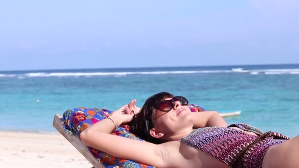 Primer plano joven mujer feliz que pone y baños de sol en la tumbona en la hermosa playa, sonriendo y soñando. Bali, Indonesia. Fondo oceánico, olas tranquilas y sol, relajarse. Full HD, 50 fps, 1080p . — Vídeos de Stock