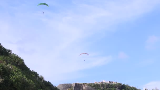 Paraglidové létají přes úžasnou horu u pláže, na ostrově Bali, v Indonésii. Krásný výhled, nebe a hora plné rostlin. Full HD, 50 fps, 1080p. — Stock video