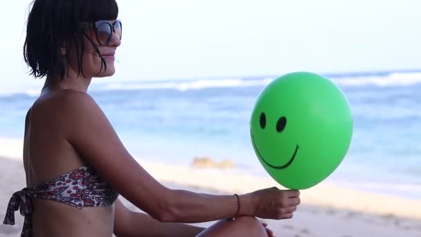 Jovem mulher sexy sentada alegremente na praia com balão verde. Bali, Indonésia. Full HD, 50fps. Perto do oceano, bela vista romântica de férias . — Vídeo de Stock