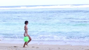 Mutlu seksi genç ince kadın gülümseme yavaş hareket ile yeşil balon ile okyanus plaj tarafındaki çalıştıran mayo. Okyanus güzel gün görünümü.