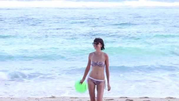 Joyeux sexy jeune femme mince en maillot de bain courant sur le côté de la plage de l'océan avec ballon vert avec sourire au ralenti. Belle vue sur l'océan jour . — Video