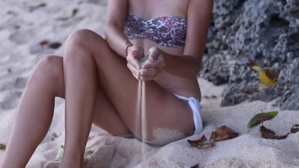 Zavřete pohled dívky rukou s bílým pískem, filtrování přes prsty, zatímco sedí na pláži. Bali, Indonésie. V blízkosti oceánu. Krásné pozadí. Čas. — Stock video