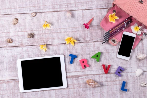 Worden stijlvol. Modieuze Ladys accessoires. Roze luxe python huid handtas, cosmetica, tablet, smartphone, bloemen van de plumeria. Detail mode is ingesteld, bovenaanzicht, houten achtergrond. Word "reizen". — Stockfoto