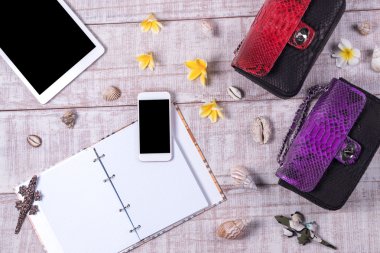 Bir moda blogger bir temel nesneleri yükü. «Ana sayfa» moda piton yılan derisi çanta, akıllı telefon, tablet pc, görünümünü kabukları. Plumeria frangipani çiçekler. Ahşap arka plan. Not defteri.