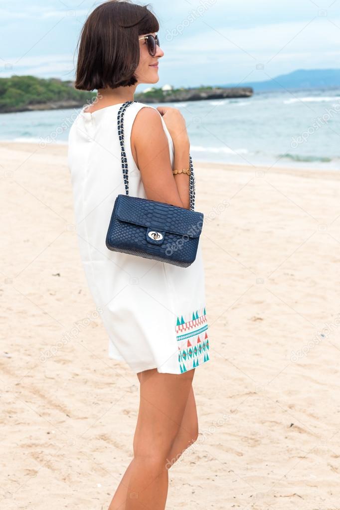 Beautiful Summer Woman with sunglasses and luxury handmade snakeskin python blue handbag. Beautiful asian background. Posing on the beach of tropical Bali island, Indonesia.