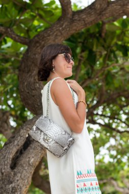 Güzel yaz kadın güneş gözlüğü ve lüks el yapımı yılan derisi python ile gri çanta. Güzel arka plan. Tropikal Bali Adası, Endonezya kumsalda poz.